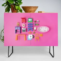 a pink cabinet with toys on it next to a potted plant