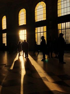 people are standing in an old building with large windows and sunlight coming through the windows