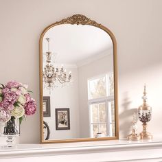 a mirror sitting on top of a mantle next to a vase with flowers in it