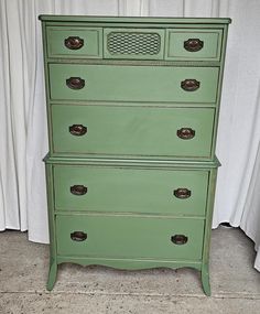 a green chest of drawers sitting on top of a floor next to a white curtain