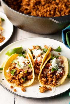 three tacos on a plate next to a pot of chili