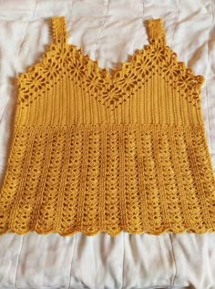 a yellow crocheted top laying on a bed