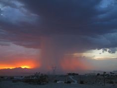 the sun is setting behind a large cloud in the sky over an arid area with power lines and telephone poles