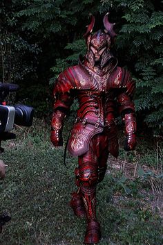 a man dressed as a demon walking in the grass with a camera next to him