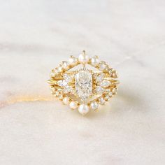 a diamond and pearl ring sitting on top of a white marble surface with gold accents