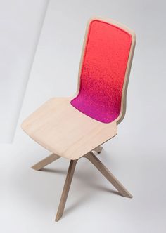 a wooden chair with a red and purple seat on it's back legs, sitting in front of a white wall