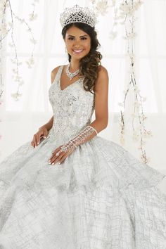 Make a grand entrance in this long glitter dress with tiered skirt by House of Wu 26921 during your Quinceanera, Sweet 16 party, or for any formal event. Sparkle under the stars with this metallic cracked ice ball gown! The sleeveless V-neck bodice features sparkling beading with front and back straps. The three-tiered ruffle skirt is accented with horsehair to add a touch of drama. This look is finished with a corset back and a gorgeous train. House of Wu Quinceanera Collection Spring 2019 Styl Charro Dress, Glitter Dress Long, Royal Blue Quinceanera Dresses, White Quince Dresses, White Quince, Xv Dresses, Quinceanera Collection, White Tulle Dress, Quinceanera Dresses Gold