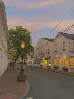 people are walking down the street in front of some shops and buildings at dusk time