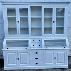 a white china cabinet with glass doors and drawers on the front, sitting against a brick wall