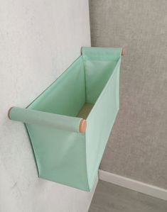 a green storage bin hanging on the wall next to a white wall with a wooden stick sticking out of it