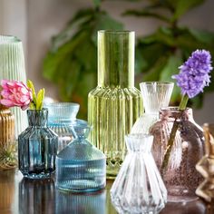 many different colored vases sitting on a table with flowers in them and one is empty