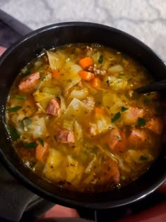 a person holding a bowl of soup with meat and vegetables in it on top of a table