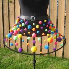 a mannequin with multi colored balls on it's skirt and belt is standing in front of a fence