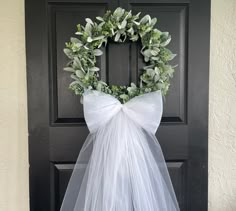 a white tulle wreath hanging on the front door with greenery and bow tied around it