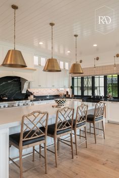 a large kitchen with white cabinets and gold pendant lights hanging from the ceiling over the island