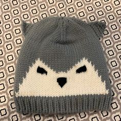 a gray and white knitted hat with a cat's face on the front