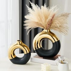 two black and gold vases sitting on top of a table next to a cup