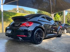 the rear end of a black sports car parked under an awning in a parking lot