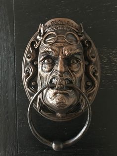 a metal door knock with a face on it's side and a ring in the middle