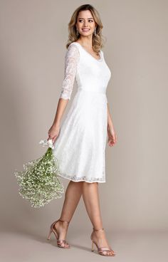 a woman in a white dress holding a bouquet of flowers and posing for the camera