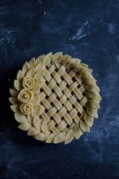 a pie crust with roses on it sitting on top of a blue countertop next to a knife and fork