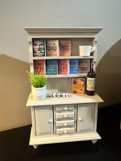 a miniature book shelf with books and a potted plant on top, next to a bottle of wine