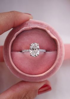 a person holding a ring in a pink velvet box with a diamond on it's side