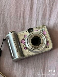 a camera sitting on top of a bed next to a white sheet with pink flowers