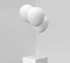 three white balloons floating in the air on top of a square stand with one balloon attached to it