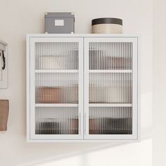 a white cabinet with glass doors next to a mirror and other items on the wall