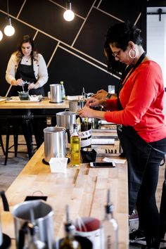 two women preparing food in a kitchen with wooden tables and hanging lights above the counter