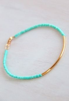 a gold plated bracelet with turquoise beads and a small beaded charm on it