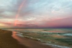 a rainbow is seen in the sky over the water at sunset on a sandy beach