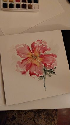 a watercolor painting of a pink flower on paper next to a brush and palette