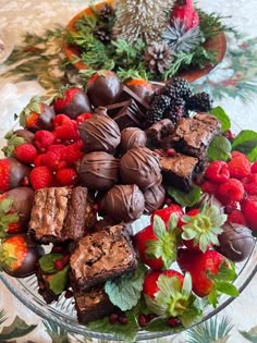 a glass bowl filled with assorted chocolates and strawberries on top of a table