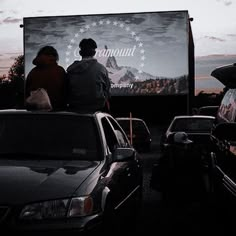 two people sitting on the back of a truck at dusk with mountains in the background