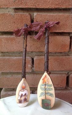 two wooden spoons with designs on them are sitting next to a brick wall and one has a bow