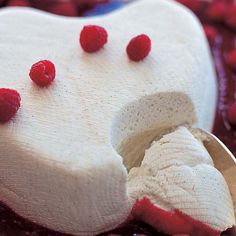 a white cake with raspberries on it and a spoon in the foreground