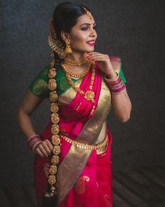 a woman in a red and green sari with gold jewelry on her neck, posing for the camera