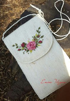 a white purse with pink flowers on it sitting on top of a piece of wood