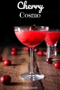 two glasses filled with cherry cosmo on top of a wooden table next to cherries