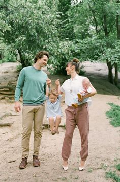 a man, woman and child are walking in the dirt with trees behind them on a sunny day