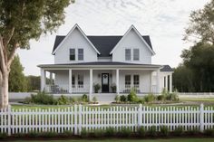 a white house with black roof and two story windows on the front porch is surrounded by greenery