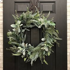 a wreath on the front door of a house with green leaves and greenery hanging from it