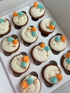 twelve cupcakes with white frosting and orange and blue decorations in a box