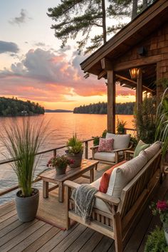 a wooden deck with two couches on it next to the water and trees at sunset