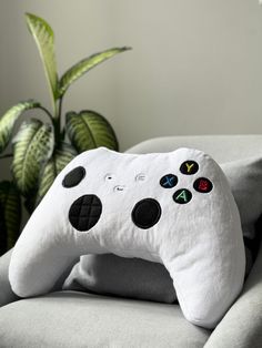 a white controller pillow sitting on top of a couch next to a potted plant