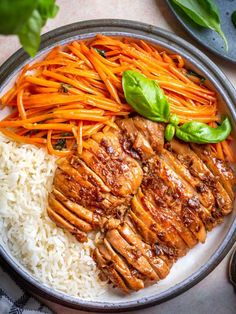 a plate with chicken, rice and carrots on it next to some basil leaves