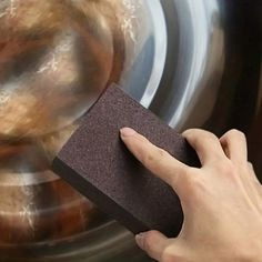 a hand holding a sponge next to a dryer door with an object in the background