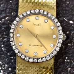 "Exquisite & polished design from the house of Piaget. This vintage 18K yellow gold watch has a classic halo round-shaped diamond bezel & markers. Enhanced by 48 round-cut factory set diamonds, prong-set, weighing approx. 1.00 carats, G-H color, VS1 Clarity.  The back is marked with Serial # 359486 with a fold-over clasp marked with the \"P\" of the brand. The band has a beautiful braided polished pattern, adding a touch of elegance. Weight: 63.5 Grams  Serial # Marked: 19706 B2 Metal: 18K Yello Formal Yellow Gold Diamond Watch With Diamond Accents, Formal Yellow Gold Diamond Watch With Accents, Elegant Yellow Gold Diamond Watch With Diamond Hour Markers, Yellow Gold Diamond Watch With Brilliant Cut For Anniversary, Diamond Watch With Brilliant Cut, Polished Diamond Watch With Round Shape, Round Diamond Watch With Polished Finish, Classic Gold Diamond Watch With Single Cut Diamonds, Elegant Diamond Watch With Pave Setting For Formal Occasions